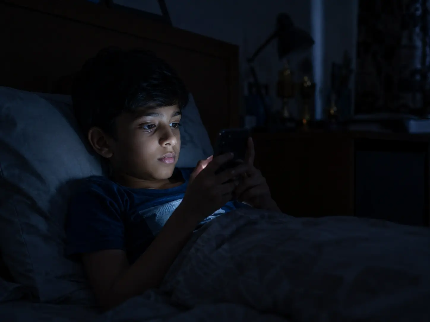 Child using smartphone in bed in a dark room
